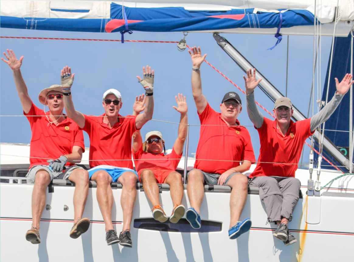 Mehrer winkende Möännger in roten T-shirts auf einem Boot sitzend und winkend