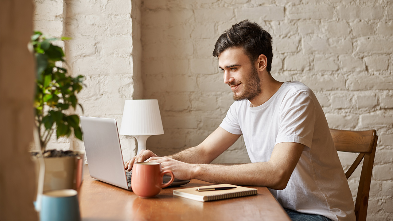 Young man is working on his laptop and smiling