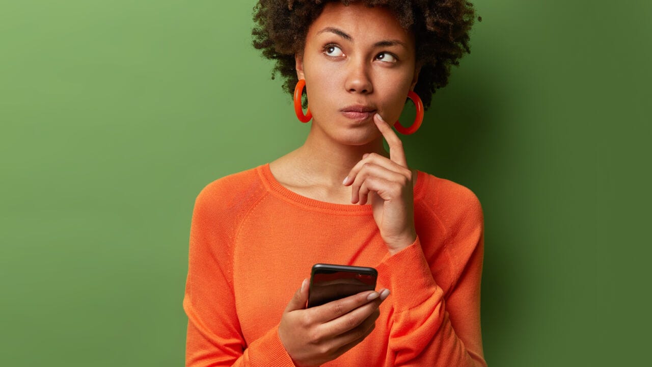 Frau mit Handy in der Hand schaut nachdenklich nach oben