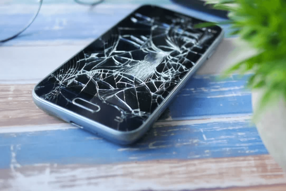 Ein Handy mit einem zersprungenem Display liegt auf einem Holztisch.