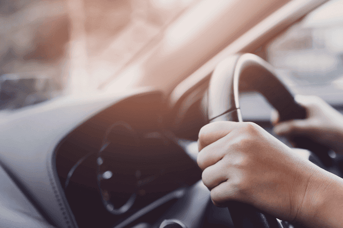 Eine Person sitzt im Auto und hat die Hände am Lenkrad.