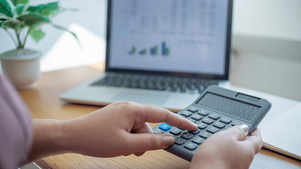 Detailansicht einer Person, die einen Taschenrechner benutzt, um Finanzdaten auf einem Laptop zu analysieren, betont die Wichtigkeit von präzisem Cashflow-Management und finanzieller Planung in einem gut beleuchteten Büro.