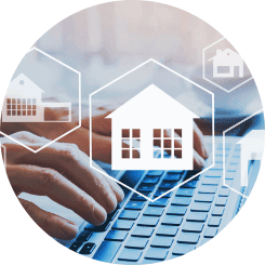 Digitale Beratung zum Immobilieninvestment: Hände tippen auf einer Laptop-Tastatur, darüber schweben durchsichtige Symbole von Häusern, die die moderne und vernetzte Immobilienberatung und -planung online visualisieren.