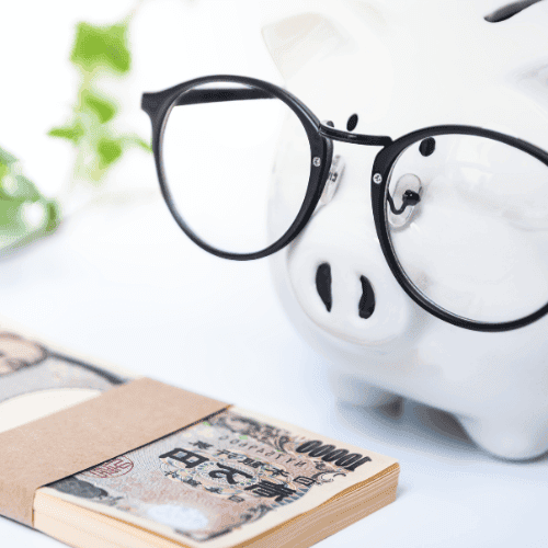 Ein kreatives Bild, das ein Sparschwein mit einer schwarzen Brille darstellt, neben einem Bündel Geldscheine. Im Hintergrund ist unscharf grünes Laub zu sehen, was auf Wachstum und finanzielle Planung anspielt.