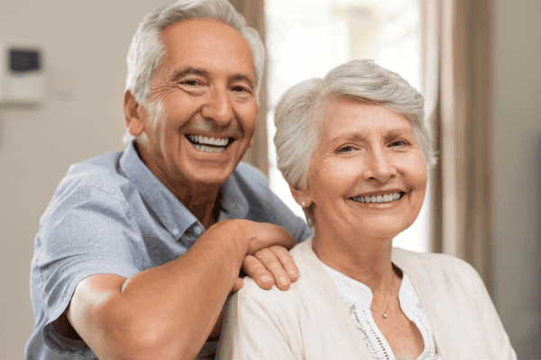Ein älteres Paar, das sich aneinander schmiegt und glücklich in die Kamera lächelt, symbolisiert einen erfüllten Ruhestand, wie er durch wohlüberlegte Altersvorsorge und Finanzplanung realisiert werden kann.