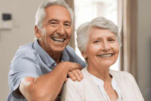Ein älteres Paar, das sich aneinander schmiegt und glücklich in die Kamera lächelt, symbolisiert einen erfüllten Ruhestand, wie er durch wohlüberlegte Altersvorsorge und Finanzplanung realisiert werden kann.