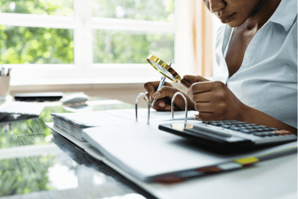 Eine professionelle Finanzberaterin analysiert Versicherungsdokumente mit einer Lupe und Taschenrechner am Schreibtisch. Dieses Bild symbolisiert die Notwendigkeit einer gründlichen Überprüfung von Finanzunterlagen im Rahmen einer professionellen Versicherungsberatung.