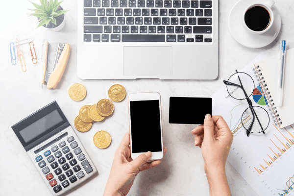 Arbeitsplatzansicht mit Laptop, Taschenrechner, Smartphone, Kreditkarte und Finanzdiagrammen auf weißem Schreibtisch, symbolisiert moderne Methoden der Ausgabenkontrolle und Finanzplanung. Ideal für Themen rund um effizientes Geldmanagement und Finanzberatung.