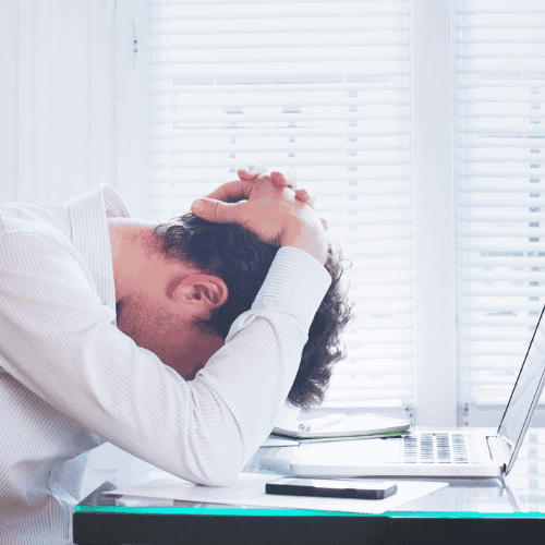Ein Bild zeigt eine Person, die vor einem geöffneten Laptop am Schreibtisch sitzt und den Kopf in Frustration in den Händen vergraben hat, was auf finanziellen Stress oder Überforderung bei der Arbeit hinweist. Das Bild kann die Notwendigkeit der Beratung zur Berufsunfähigkeitsversicherung illustrieren, um solchen Situationen vorzubeugen und finanzielle Sicherheit im Falle einer Berufsunfähigkeit zu gewährleisten.
