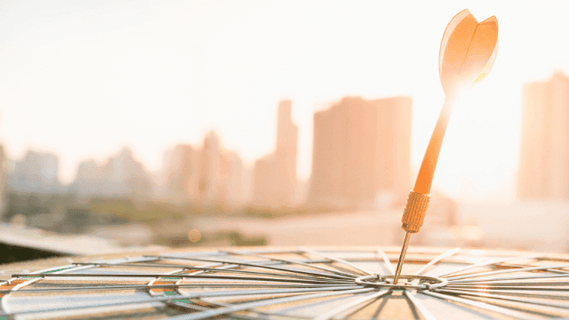 Pfeil zentral im Ziel eines Dartboards mit städtischer Skyline im Hintergrund, symbolisiert präzise Finanzplanung und das Erreichen finanzieller Ziele.