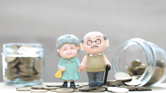 Miniaturfiguren eines älteren Paares stehen auf Münzen vor einem Geldglas, symbolisieren effektive Altersvorsorge und langfristiges Sparen.