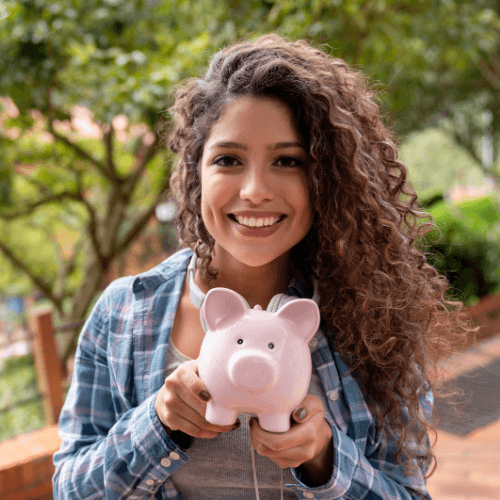 Lächelnde junge Frau mit lockigen Haaren, die ein rosa Sparschwein hält, symbolisch für Finanzplanung und Sparen.