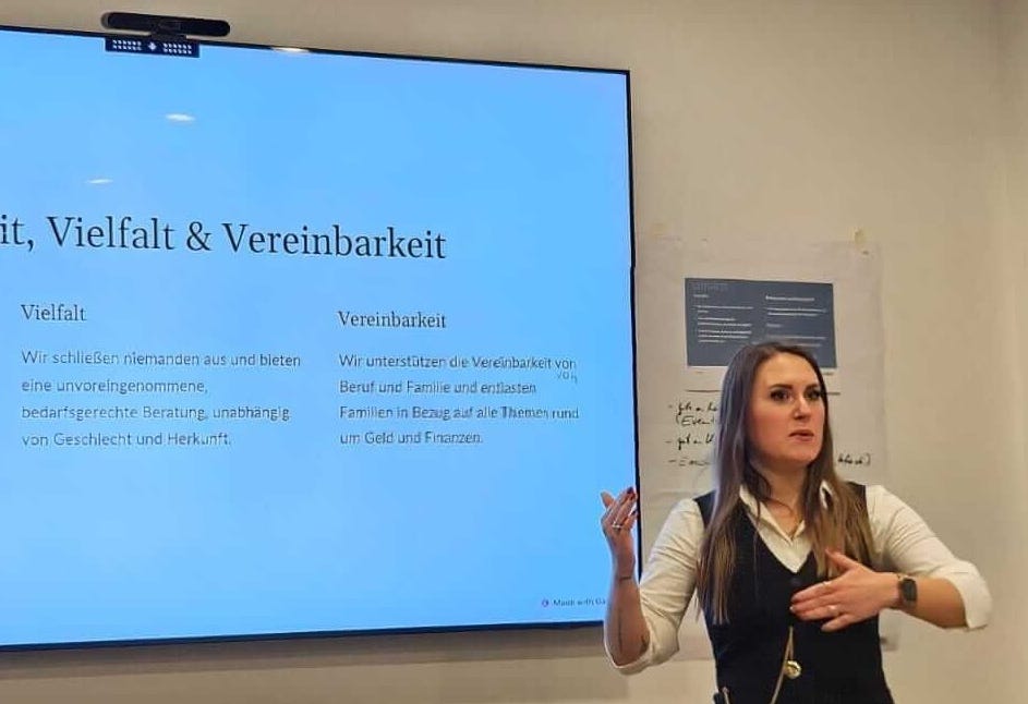 Sandra Lekarczyk, Finanzberaterin, gibt eine Präsentation über Gleichheit, Vielfalt und Vereinbarkeit, hervorgehoben durch einen Präsentationsbildschirm mit entsprechenden Stichpunkten. Sie betont die Bedeutung der Einbeziehung aller Geschlechter und Herkünfte sowie der Vereinbarkeit von Beruf und Familie im Kontext von Finanzen und Geldmanagement.