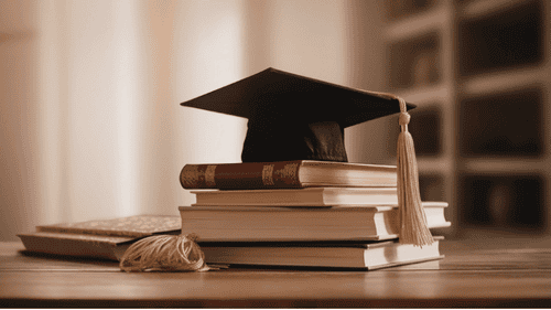 Symbolbild für Finanzberatung für Berufseinsteiger – Abschlussmütze auf Büchern steht für akademischen Karrierestart und strategische Finanzplanung ab dem Studienabschluss