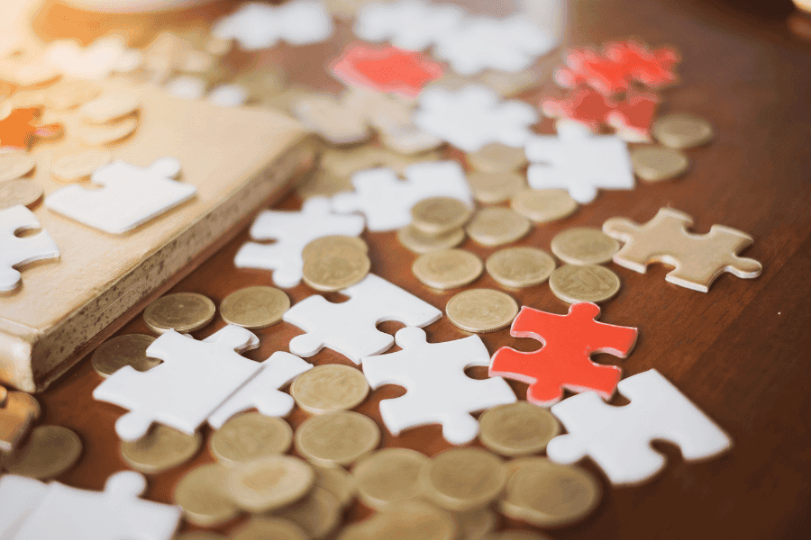 Puzzle-Teile und Münzen als Symbol für individuelle Finanzplanung – ganzheitlicher Vermögensaufbau durch passende Finanzbausteine, Struktur und ein persönliches Finanzkonzept