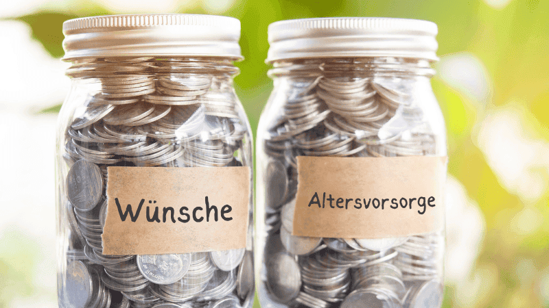 Zwei Glas-Sparschweine gefüllt mit Münzen, beschriftet mit 'Wünsche' und 'Altersvorsorge' auf einem sonnigen Tisch, symbolisieren die Wichtigkeit der finanziellen Planung und das Sparen für kurzfristige Wünsche und langfristige Ziele wie die Rente.