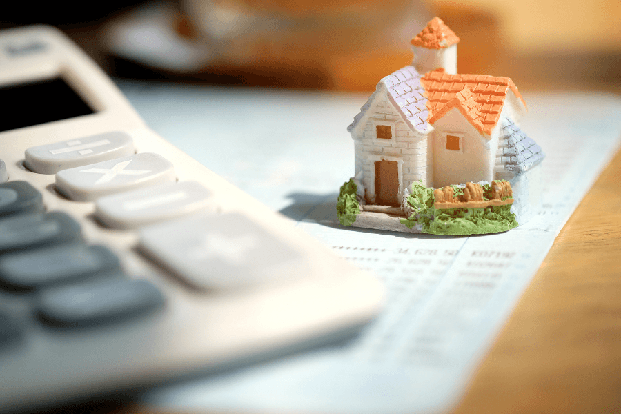 Anlageimmobilie als Kapitalanlage: Hausmodell und Taschenrechner stehen für Immobilienfinanzierung, Vermögensaufbau, Diversifikation und langfristige Investmentstrategie.